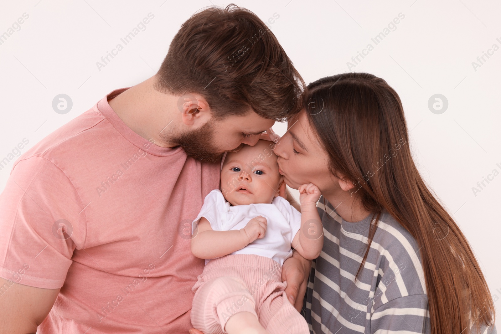 Photo of Happy family. Parents kissing their cute baby on light background
