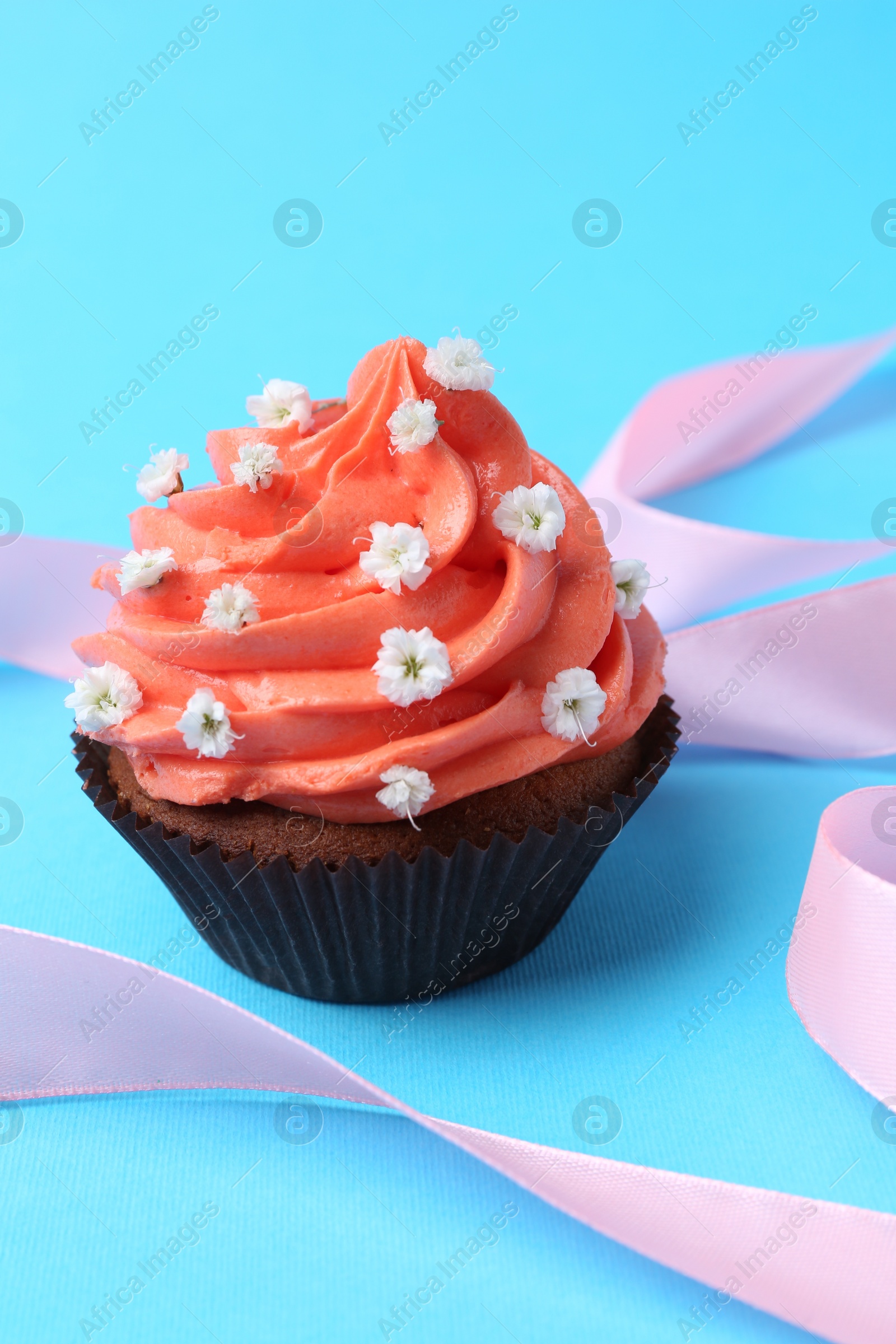 Photo of Delicious cupcake with bright cream and flowers on light blue background