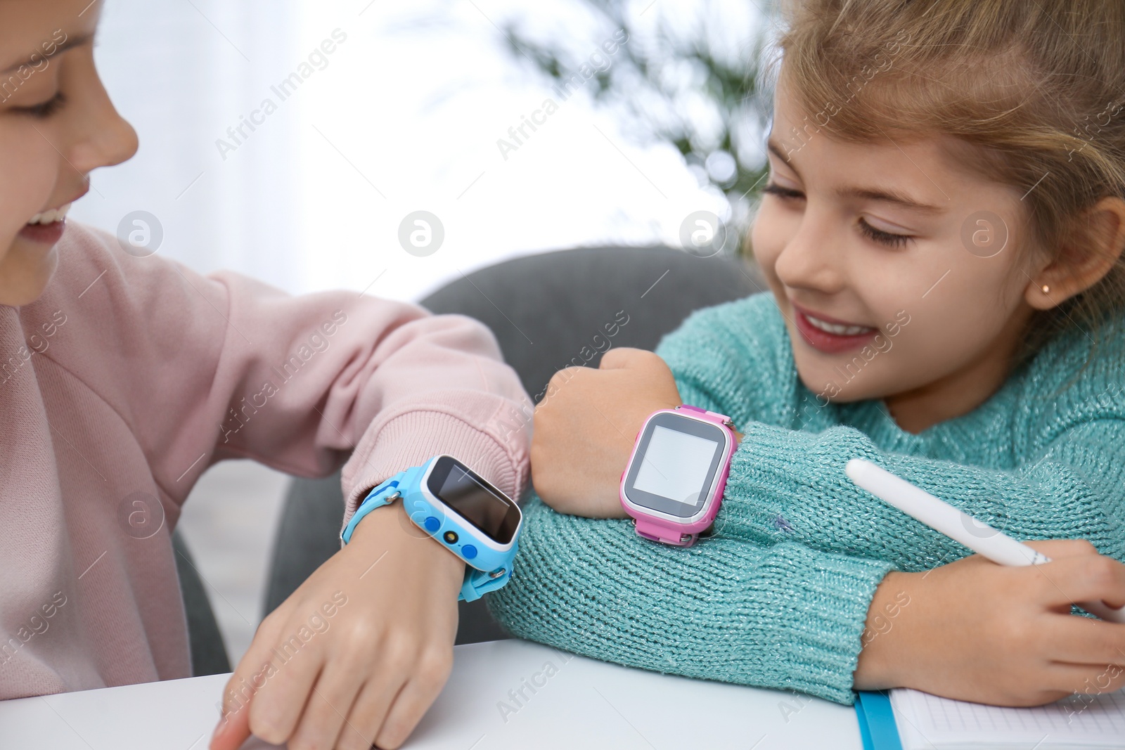 Photo of Girls with stylish smart watches at table indoors, closeup