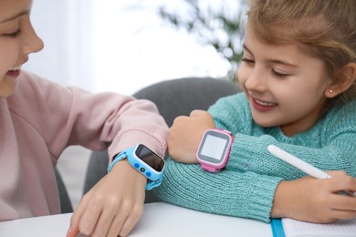 Girls with stylish smart watches at table indoors, closeup