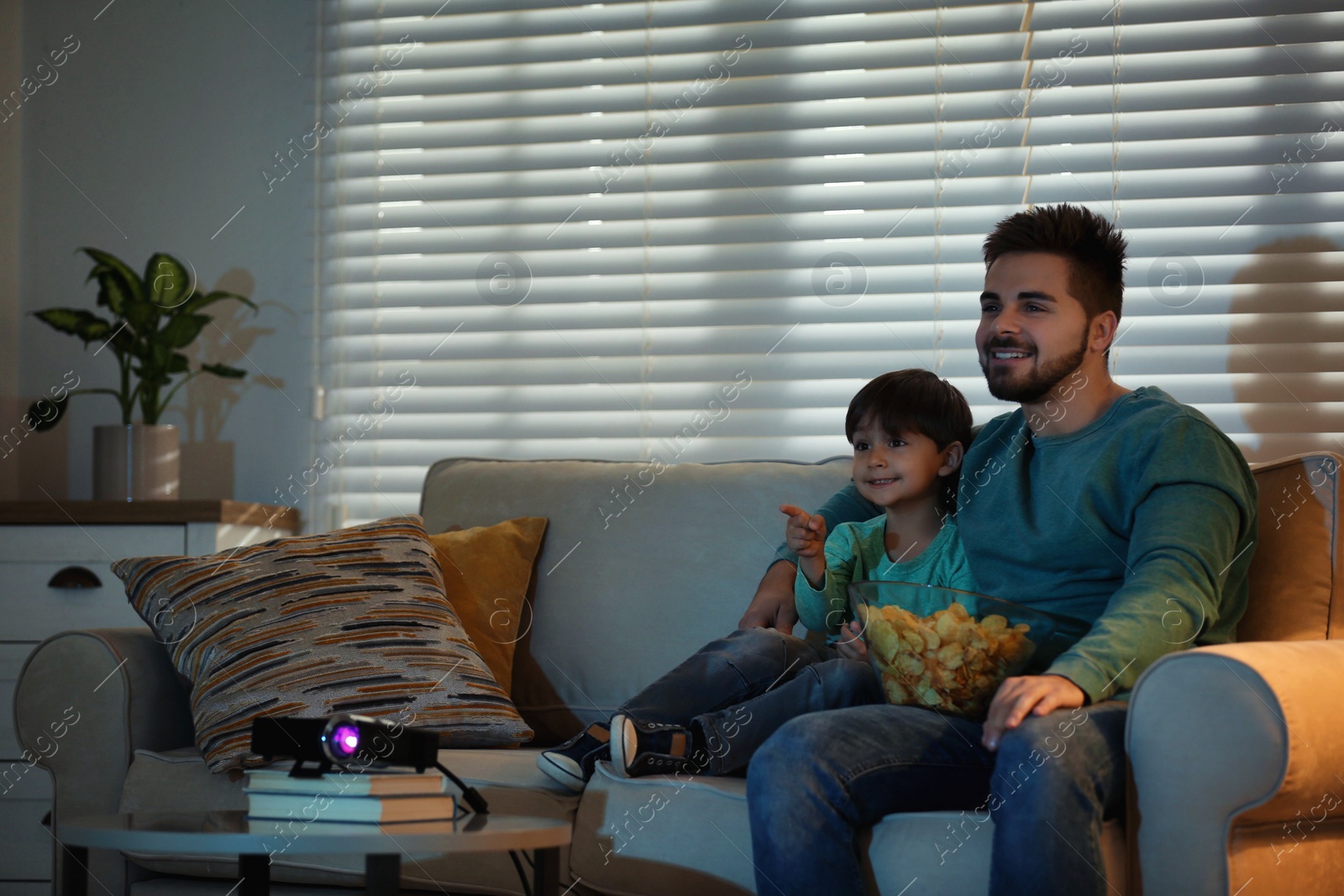 Photo of Young man and his son watching movie using video projector at home. Space for text