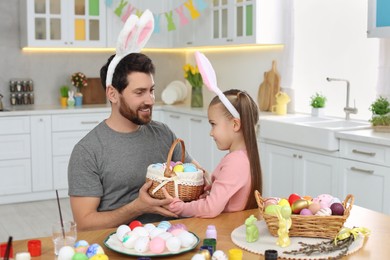 Photo of Father and his cute daughter with wicker basket full of Easter eggs in kitchen