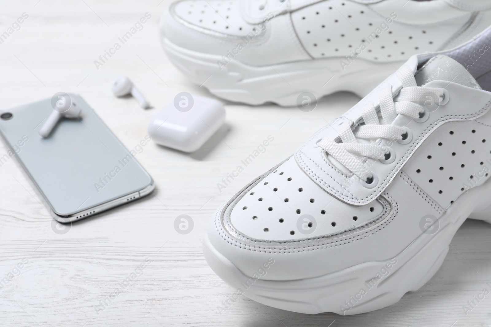 Photo of Pair of stylish sneakers, modern smartphone and wireless earphones on white wooden table, closeup