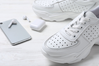 Pair of stylish sneakers, modern smartphone and wireless earphones on white wooden table, closeup