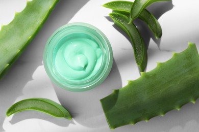 Jar with cream and cut aloe leaves on white table, flat lay