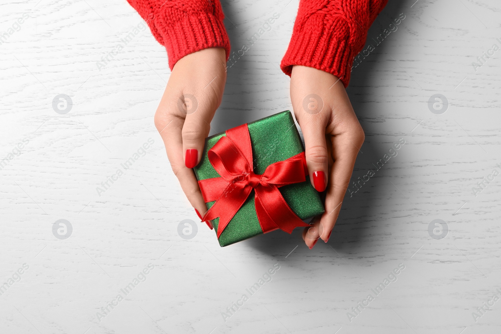 Photo of Christmas present. Woman with gift box at white wooden table, top view