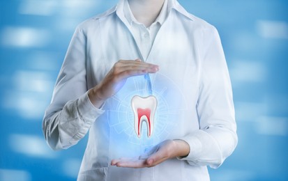 Dentist showing virtual model of tooth on light blue background, closeup