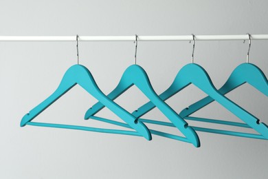 Photo of Empty turquoise clothes hangers on metal rail against light grey background