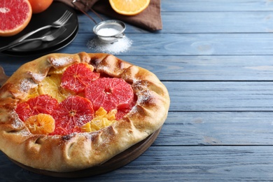 Delicious galette with citrus fruits on blue wooden table, closeup. Space for text