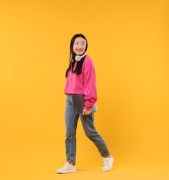 Photo of Portrait of smiling woman with headphones and laptop on orange background