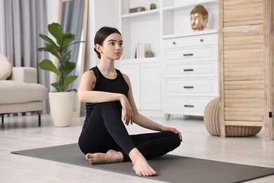 Beautiful girl sitting on yoga mat at home