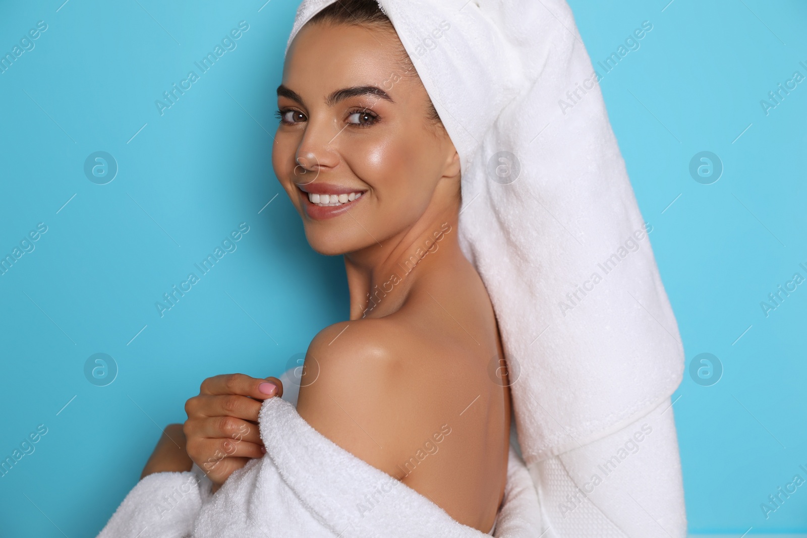 Photo of Beautiful young woman wearing bathrobe and towel on head against light blue background