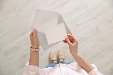 Woman holding envelope and blank greeting card indoors, top view