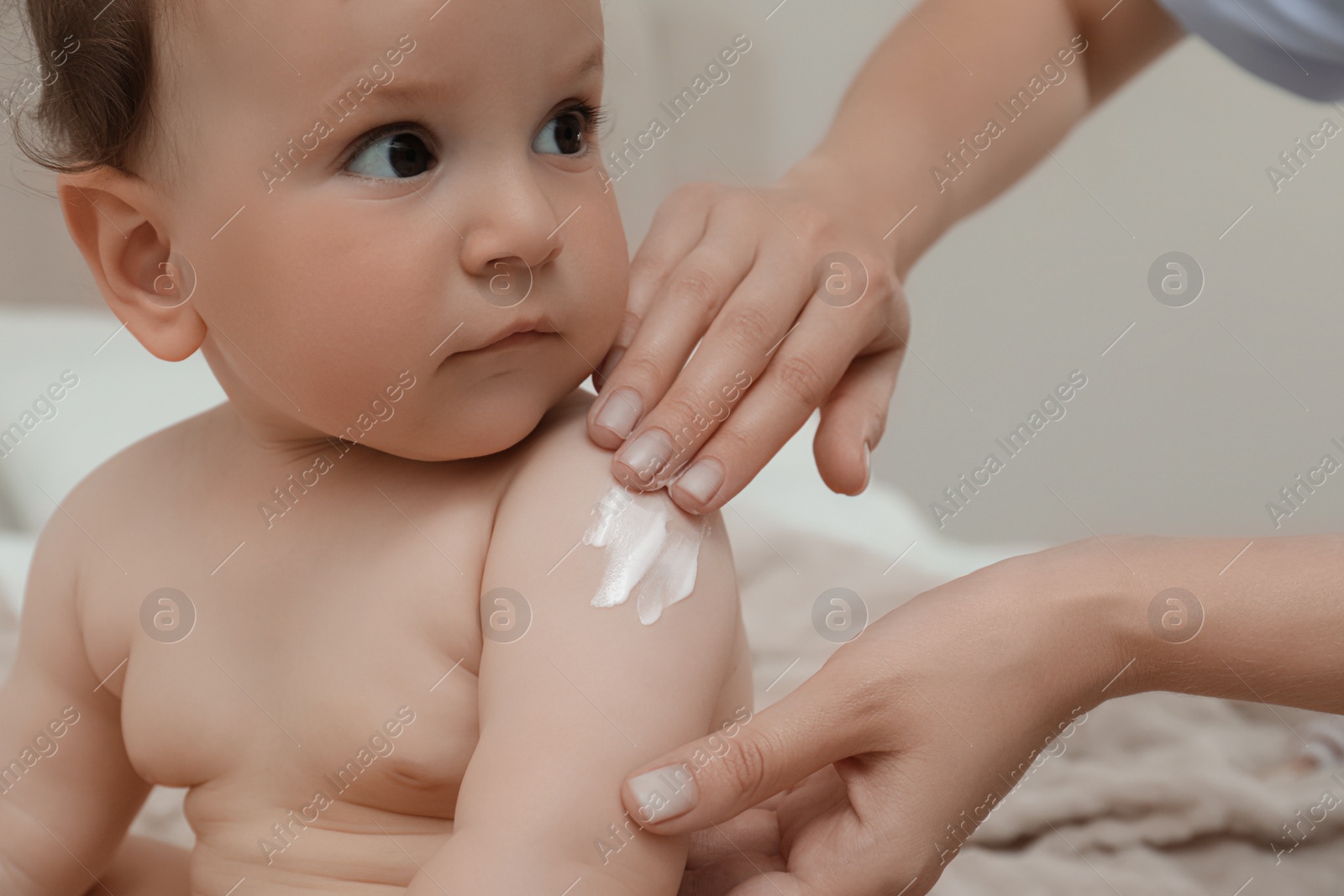 Photo of Mother applying body cream on her baby indoors, closeup