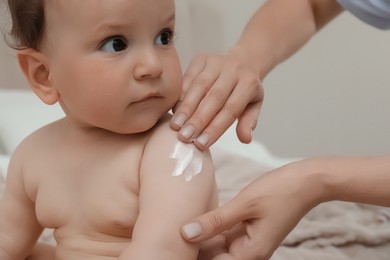 Mother applying body cream on her baby indoors, closeup