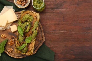 Photo of Freshly baked pesto bread with basil and cheese on wooden table, flat lay. Space for text