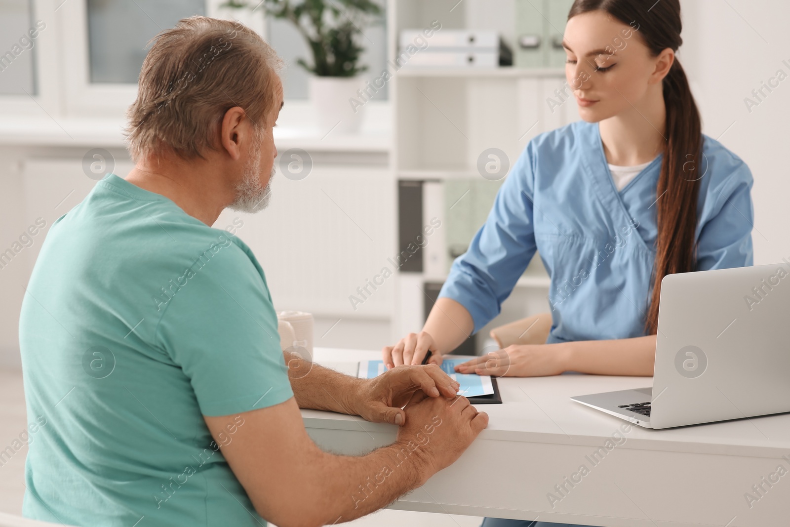 Photo of Professional orthopedist consulting patient at table in clinic