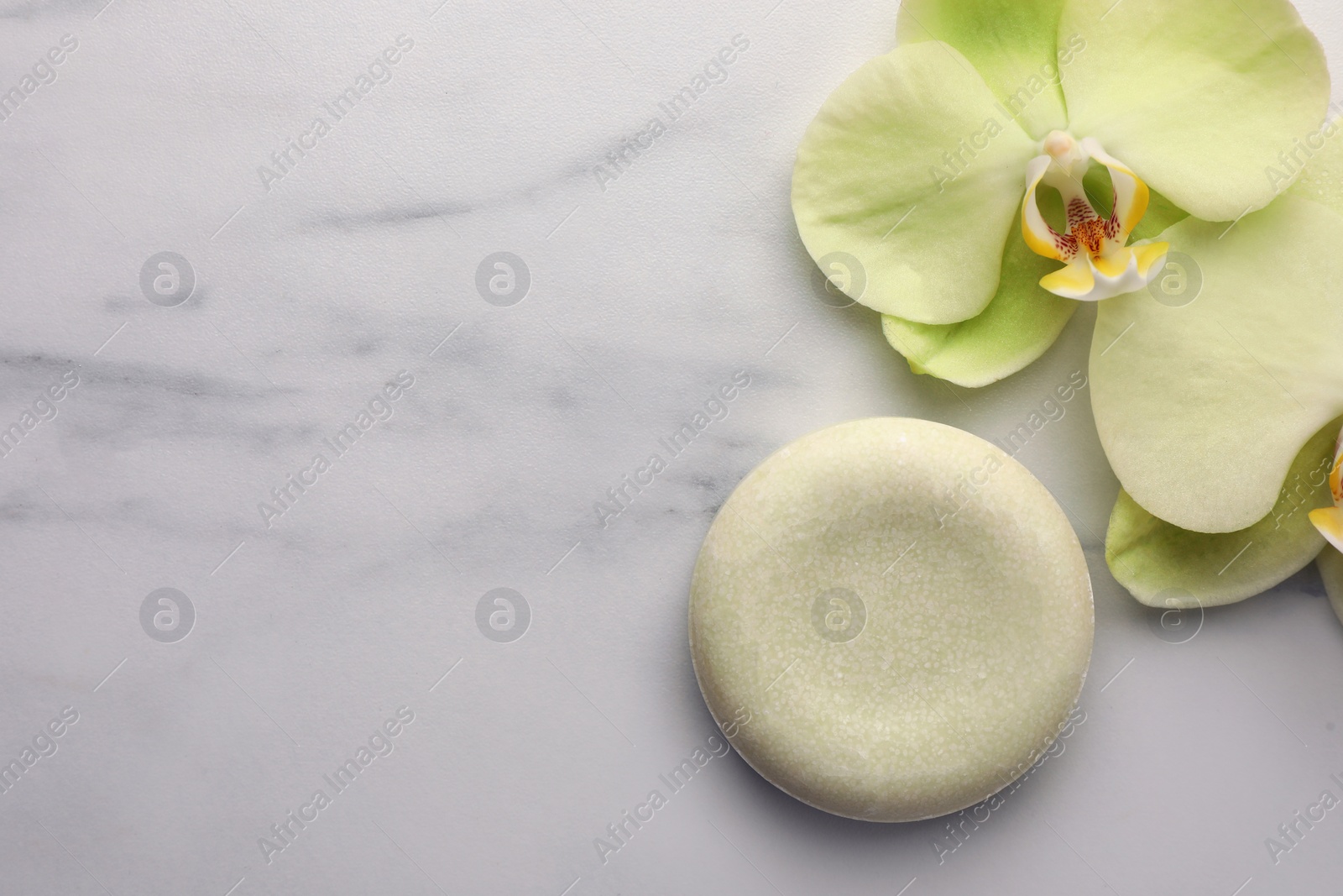 Photo of Solid shampoo bar and orchid flowers on white marble table, flat lay with space for text. Spa composition