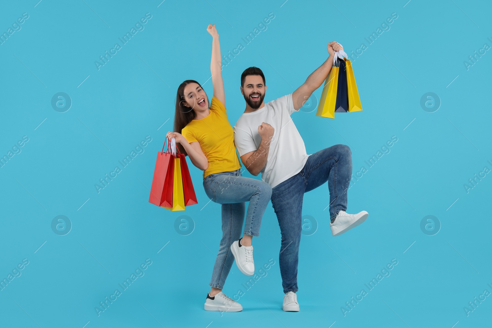 Photo of Happy couple with shopping bags having fun on light blue background