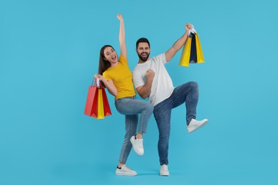 Photo of Happy couple with shopping bags having fun on light blue background