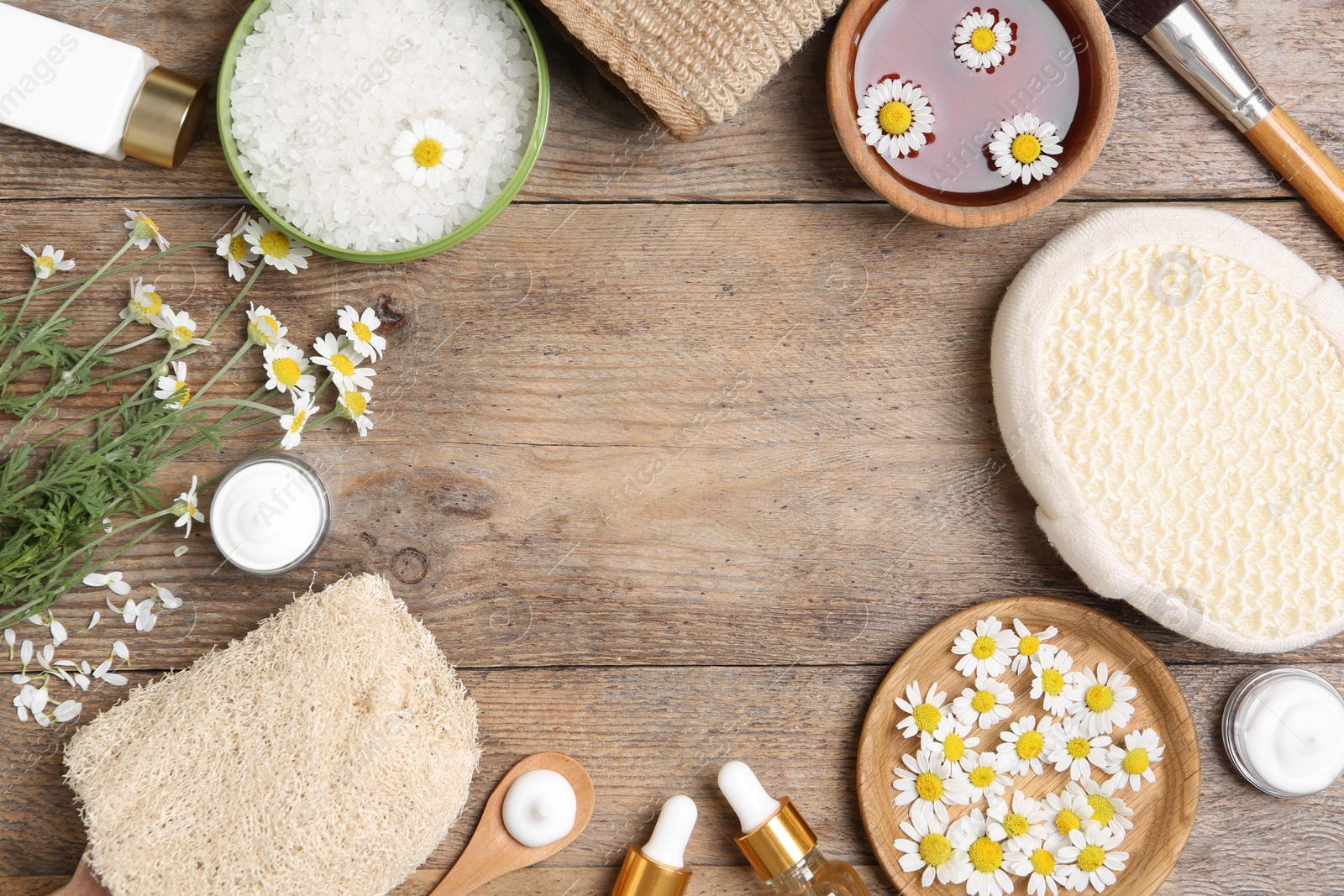 Photo of Flat lay composition with different cosmetic products, chamomile flowers and beauty accessories on wooden table. Space for text