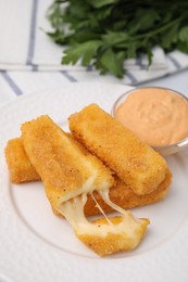 Photo of Plate with tasty fried mozzarella sticks and sauce on table, closeup