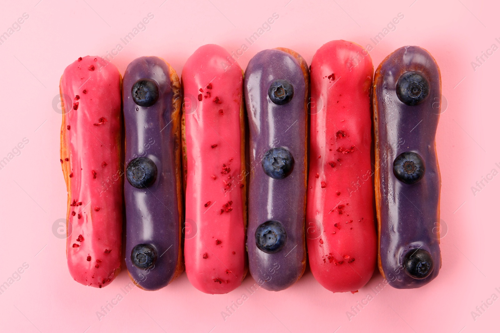 Photo of Delicious eclairs covered with glaze on pink background, top view