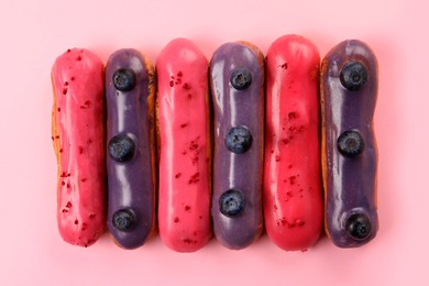 Delicious eclairs covered with glaze on pink background, top view