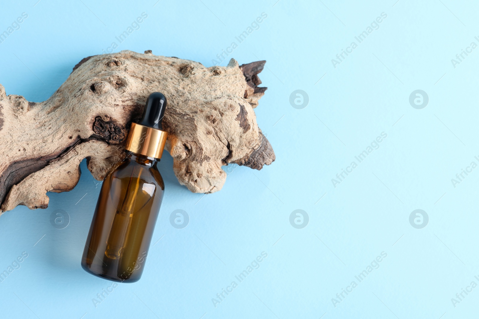 Photo of Bottle with cosmetic oil and wooden snag on light blue background, flat lay. Space for text