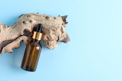 Photo of Bottle with cosmetic oil and wooden snag on light blue background, flat lay. Space for text