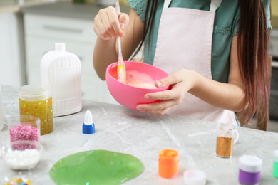 Little girl mixing ingredients with silicone spatula at table indoors, closeup. DIY slime toy