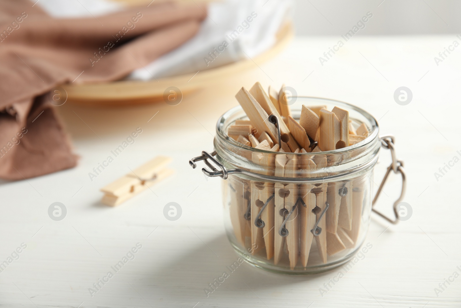 Photo of Many wooden clothespins in glass jar on white table, space for text