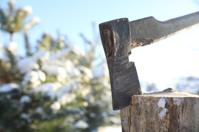 Metal axe in wooden log outdoors on sunny winter day, closeup. Space for text