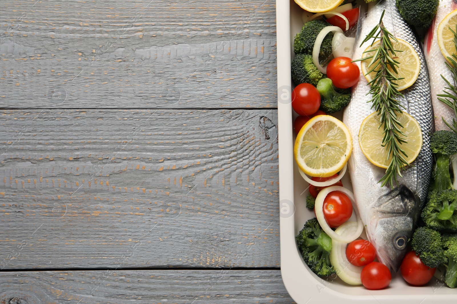 Photo of Raw fish with vegetables and lemon in baking dish on grey wooden table, top view. Space for text