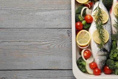 Photo of Raw fish with vegetables and lemon in baking dish on grey wooden table, top view. Space for text