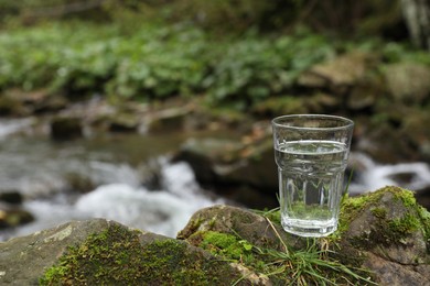 Photo of Glass of fresh water on stone with moss near stream. Space for text