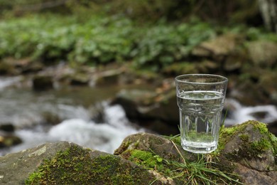 Glass of fresh water on stone with moss near stream. Space for text