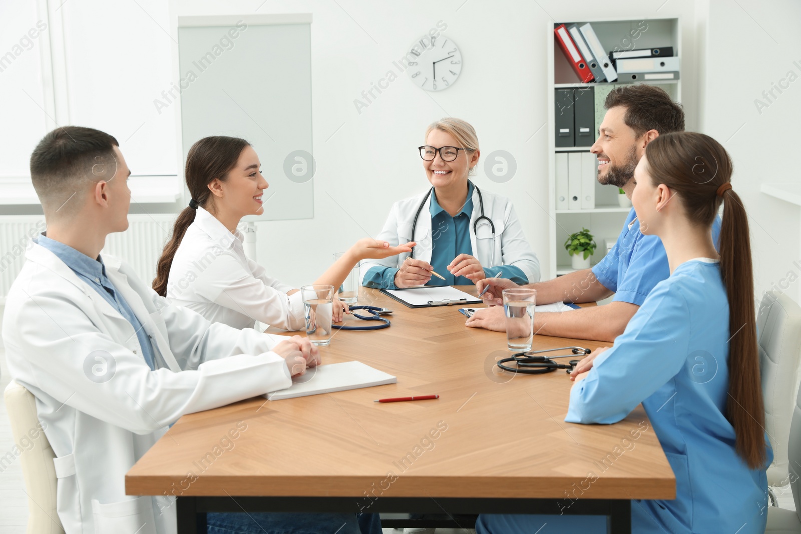 Photo of Medical conference. Team of doctors having discussion with speaker at wooden table in clinic