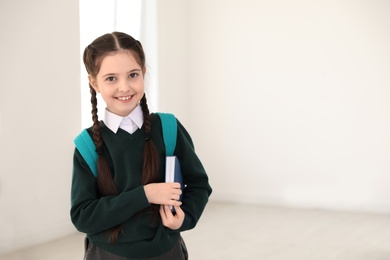 Photo of Portrait of cute girl in school uniform with backpack and book indoors. Space for text