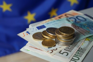 Photo of Coins and banknotes on table against European Union flag, closeup
