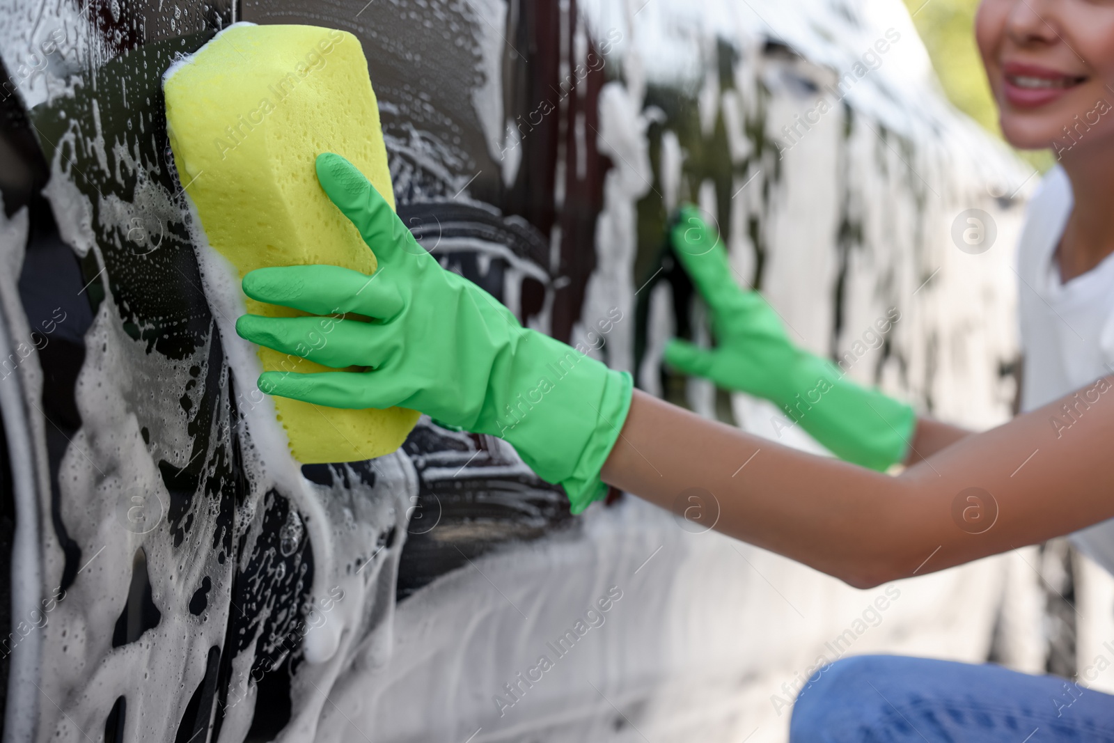 Photo of Woman washing car with sponge outdoors, closeup