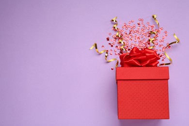 Photo of Red gift box with sequins and streamers on lilac background, flat lay. Space for text