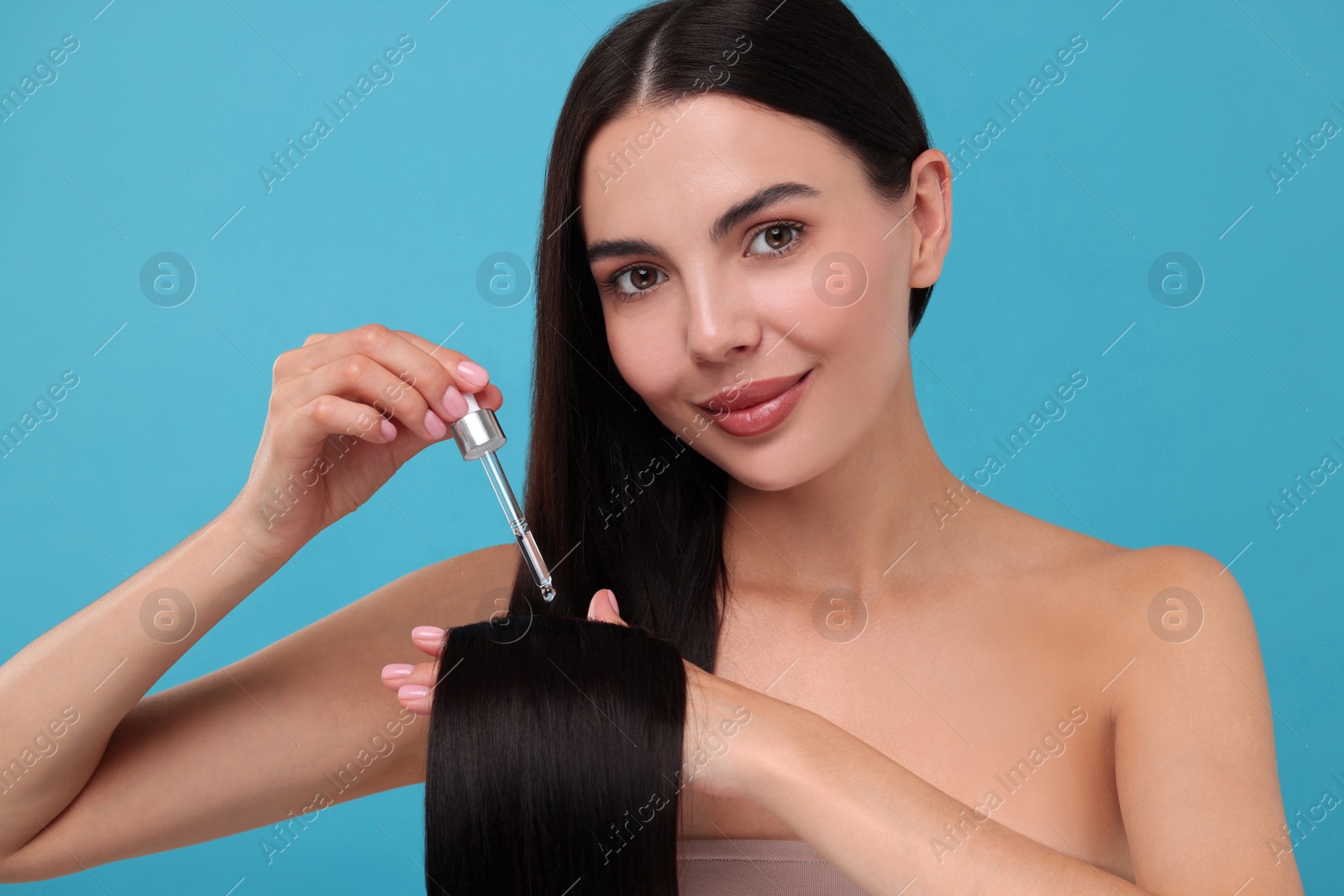 Photo of Beautiful woman applying hair serum on light blue background. Cosmetic product