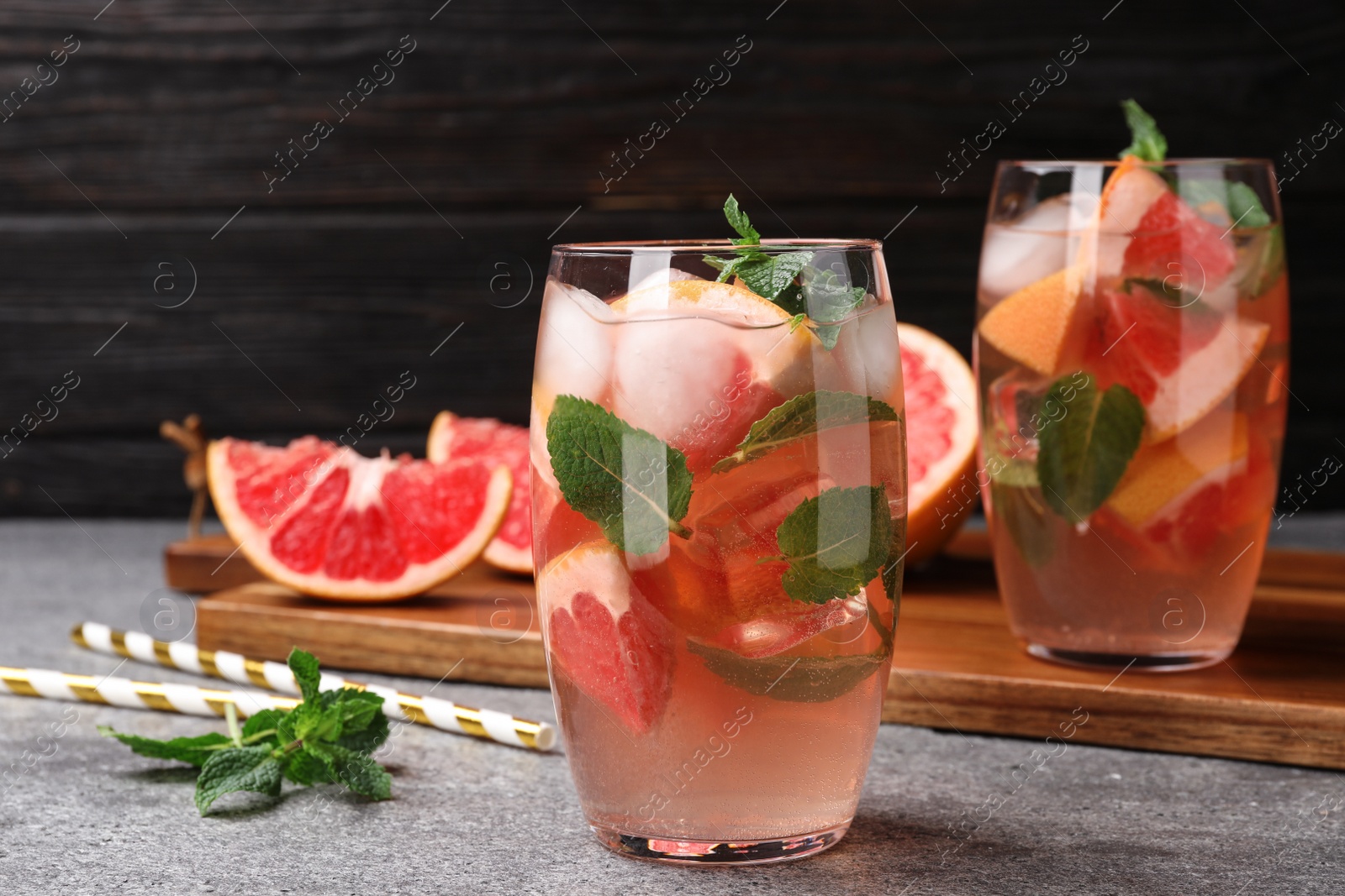 Photo of Glass of refreshing drink with grapefruit and mint on grey stone table against dark background, space for text