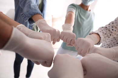 People in white medical gloves joining fists on light background, closeup