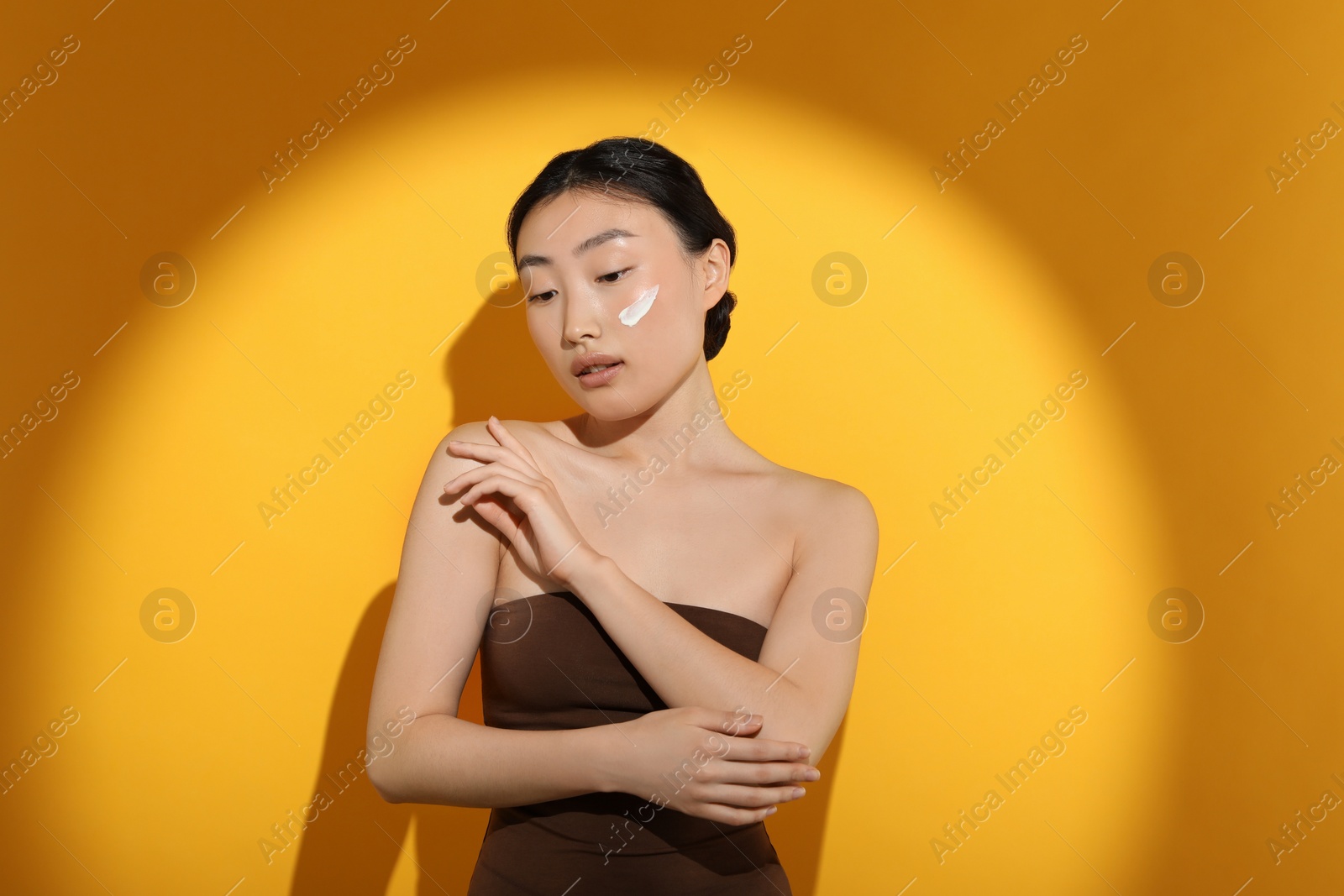 Photo of Beautiful young woman in sunlight with sun protection cream on her face against orange background