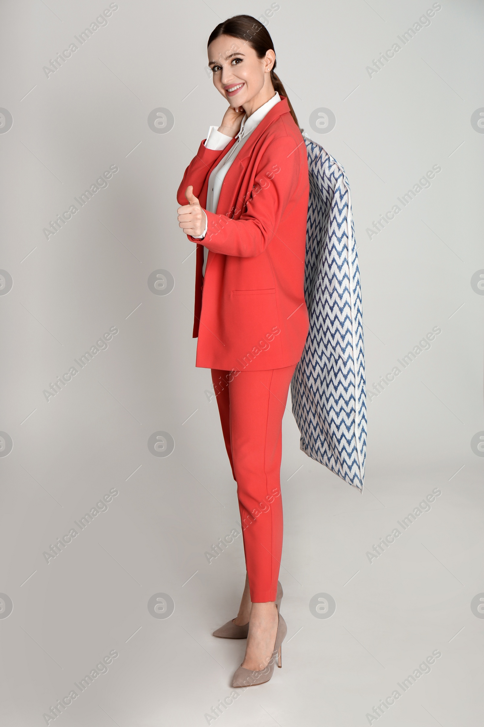 Photo of Young woman holding hanger with clothes in garment cover on light grey background. Dry-cleaning service