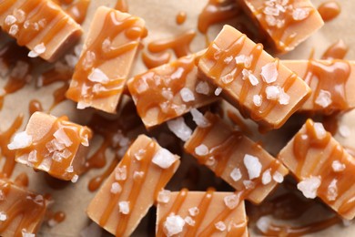 Photo of Yummy candies with caramel sauce and sea salt on parchment paper, flat lay