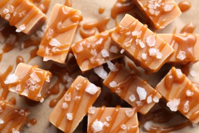 Yummy candies with caramel sauce and sea salt on parchment paper, flat lay