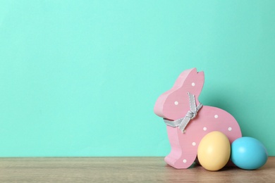 Photo of Cute wooden Easter bunny and dyed eggs on table against color background, space for text